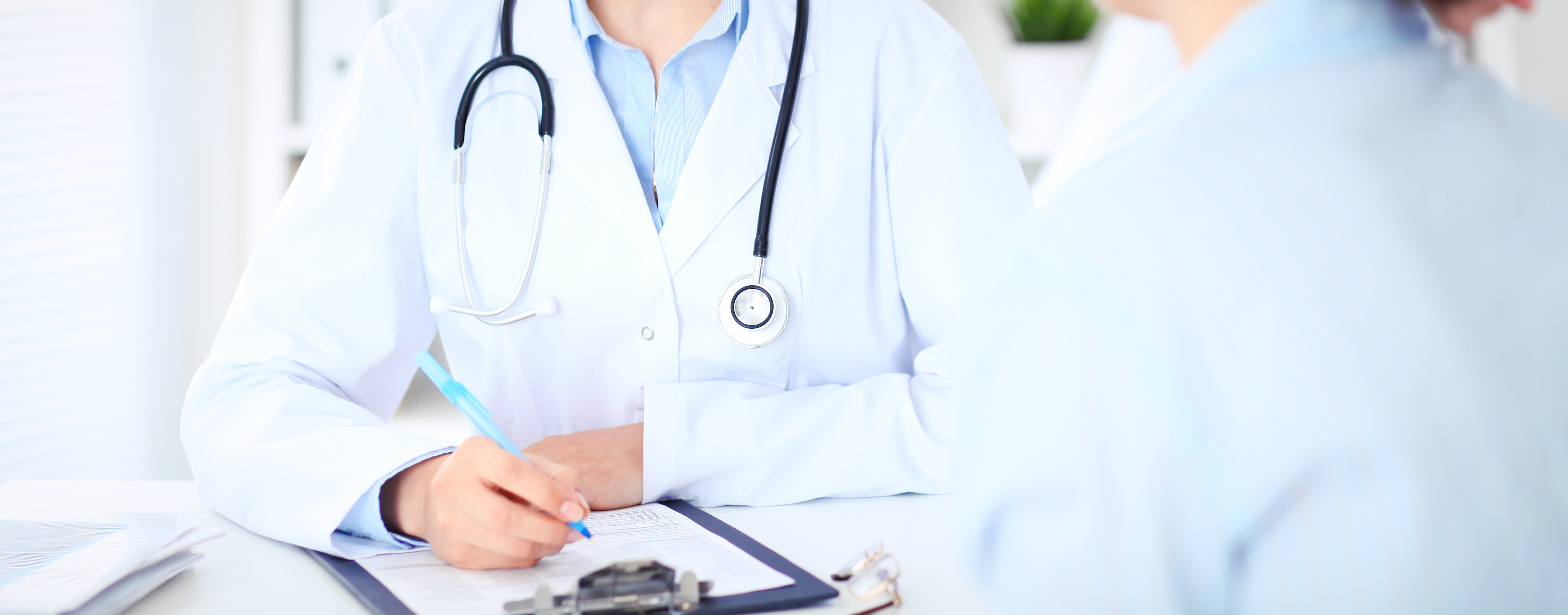 Unknown female doctor and patient discussing something while sitting at the table at hospital. Medicine and healthcare concepts.